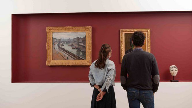 une femme et un homme de dos regardant des tableaux sur un fond rouge